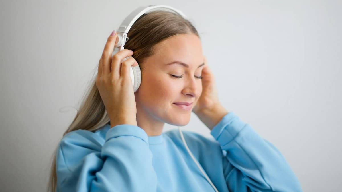 A serene young woman enjoying music with headphones on a neutral background.