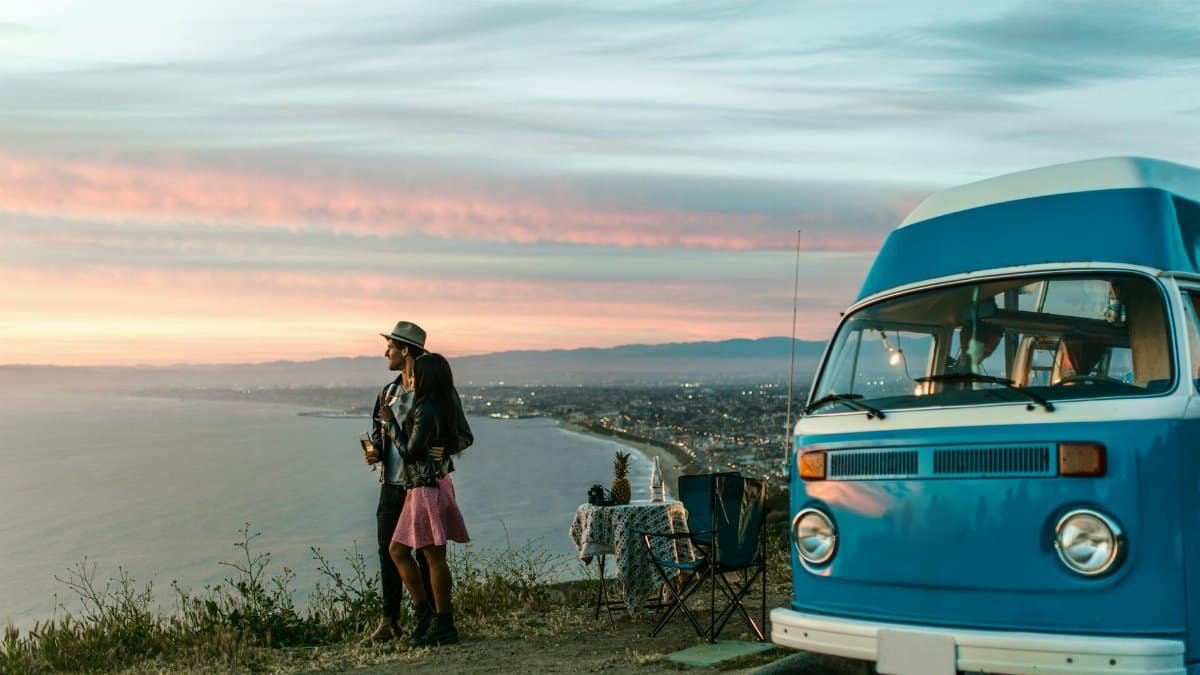 Couple enjoying a sunset view by the ocean with a camper van, evoking adventure and tranquility.