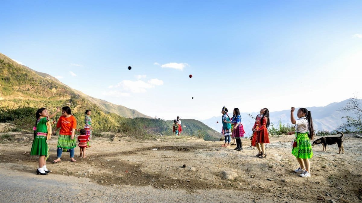 Group of local Asian children standing opposite each other and throwing balls in air while playing near mountainous area