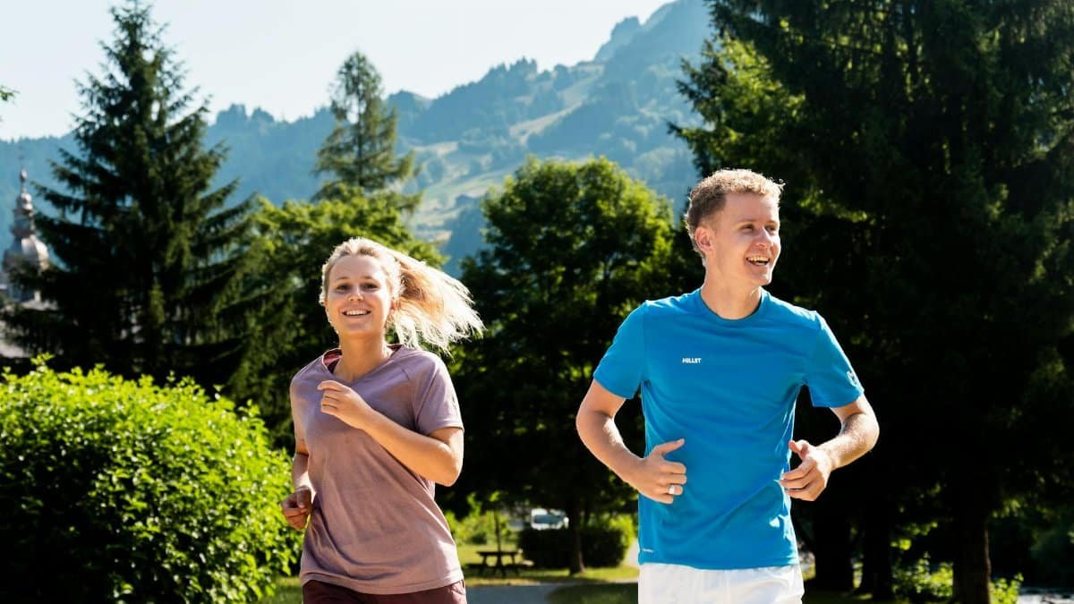 A cheerful couple jogging on a sunny day in a picturesque mountain landscape.