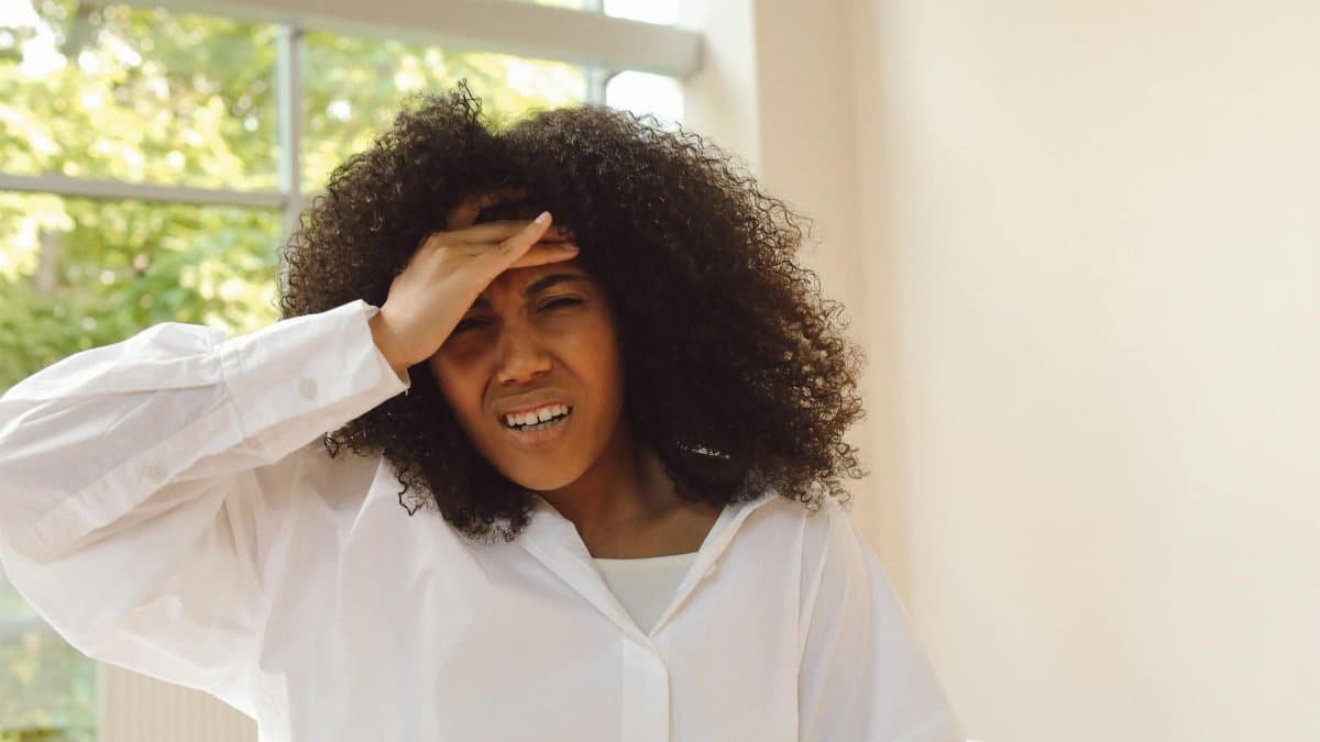 African American woman experiencing headache, holding forehead in discomfort indoors.