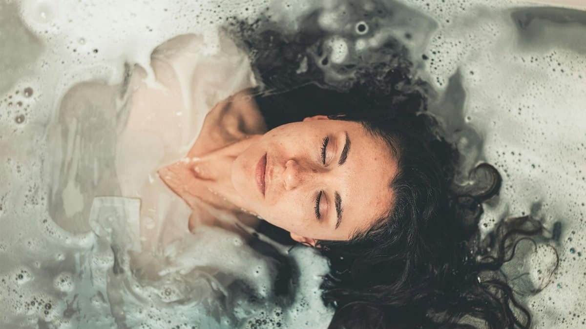 Woman with long hair enjoying a peaceful bubble bath with eyes closed, illustrating relaxation.