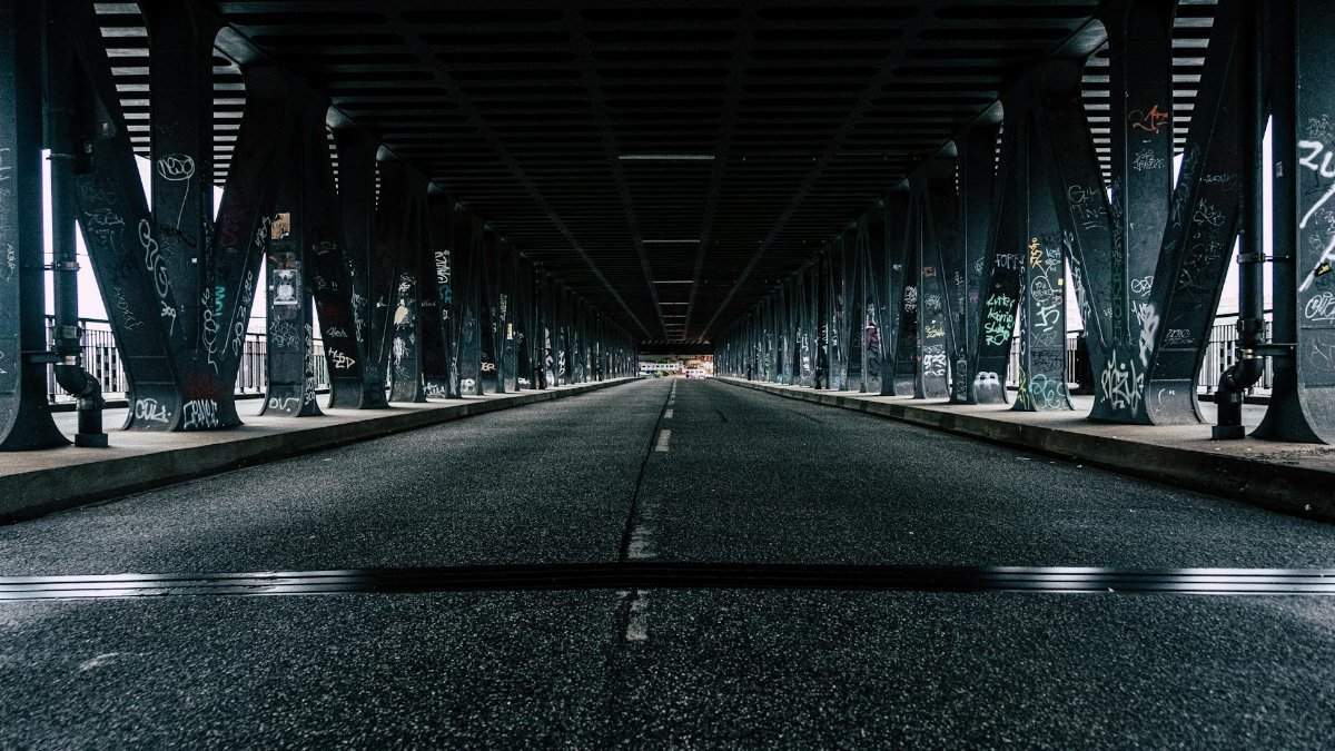 Long dark bridge with graffiti on support, highlighting urban street atmosphere.