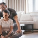 Elderly couple engaging in a yoga session indoors, practicing bound angle pose with focus and support.