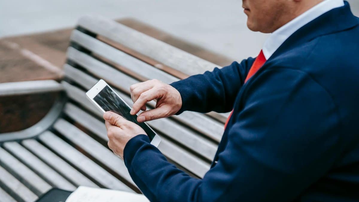 A professional man in a suit uses a tablet outdoors, showcasing modern technology in a casual setting.