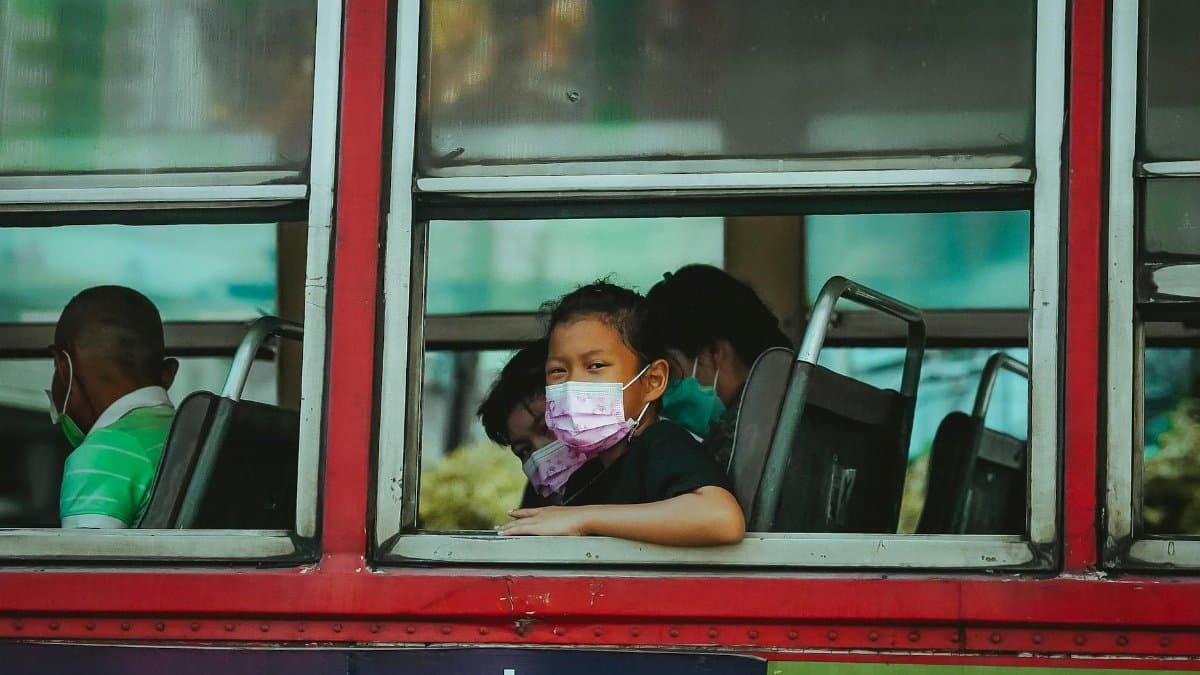 A young child wearing a face mask on a bus in Bangkok, Thailand, highlighting public transportation during pandemic times.