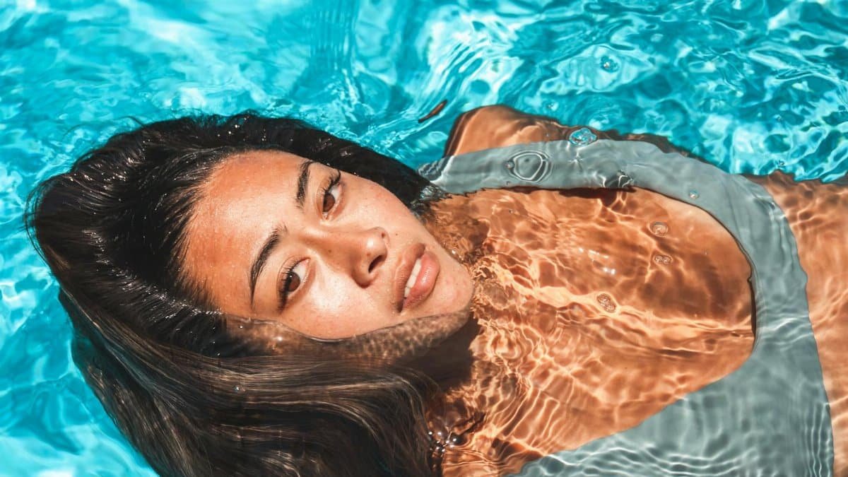Close-up of a woman relaxing in a clear blue swimming pool under bright sunlight.
