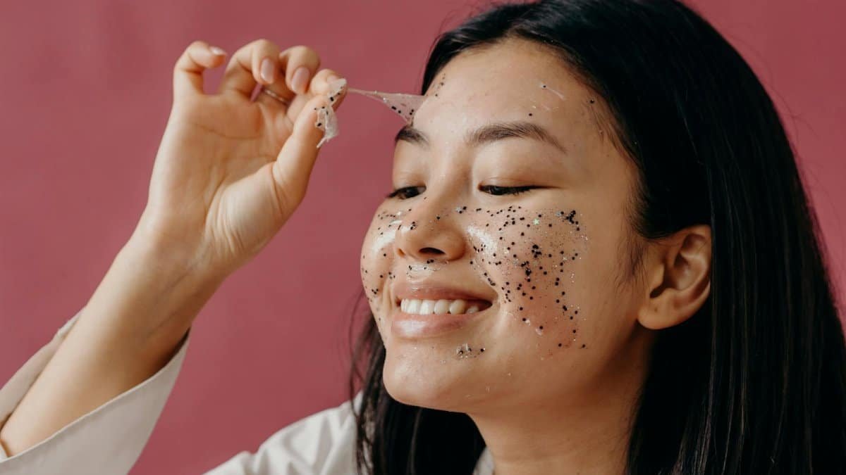 Close-up of smiling Asian woman peeling off a glittery face mask, highlighting her skincare routine.