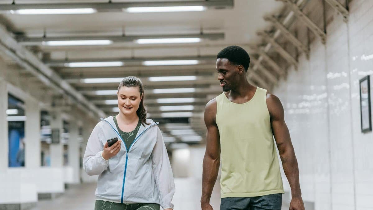A black man and a caucasian woman walking in a subway, both smiling and holding phones.