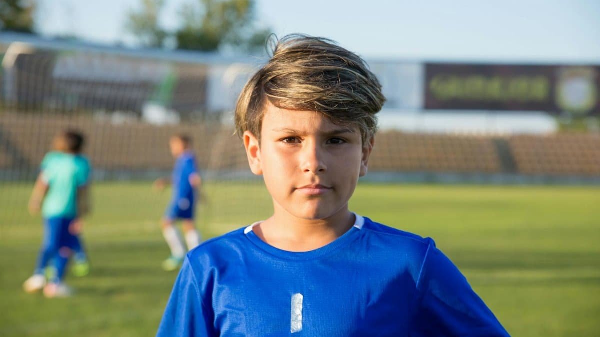 A young boy stands on a soccer field in Portugal, ready for practice under clear skies.