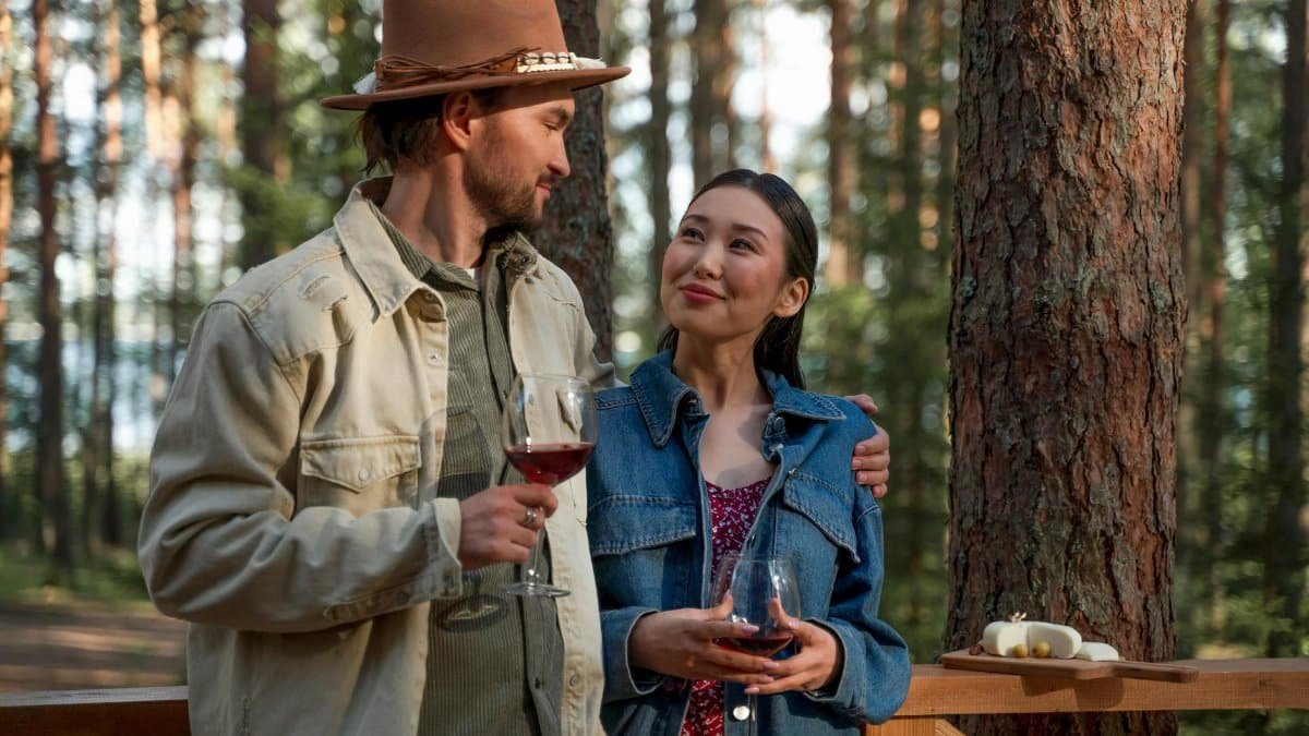 A couple shares a romantic moment drinking wine in a serene forest setting.