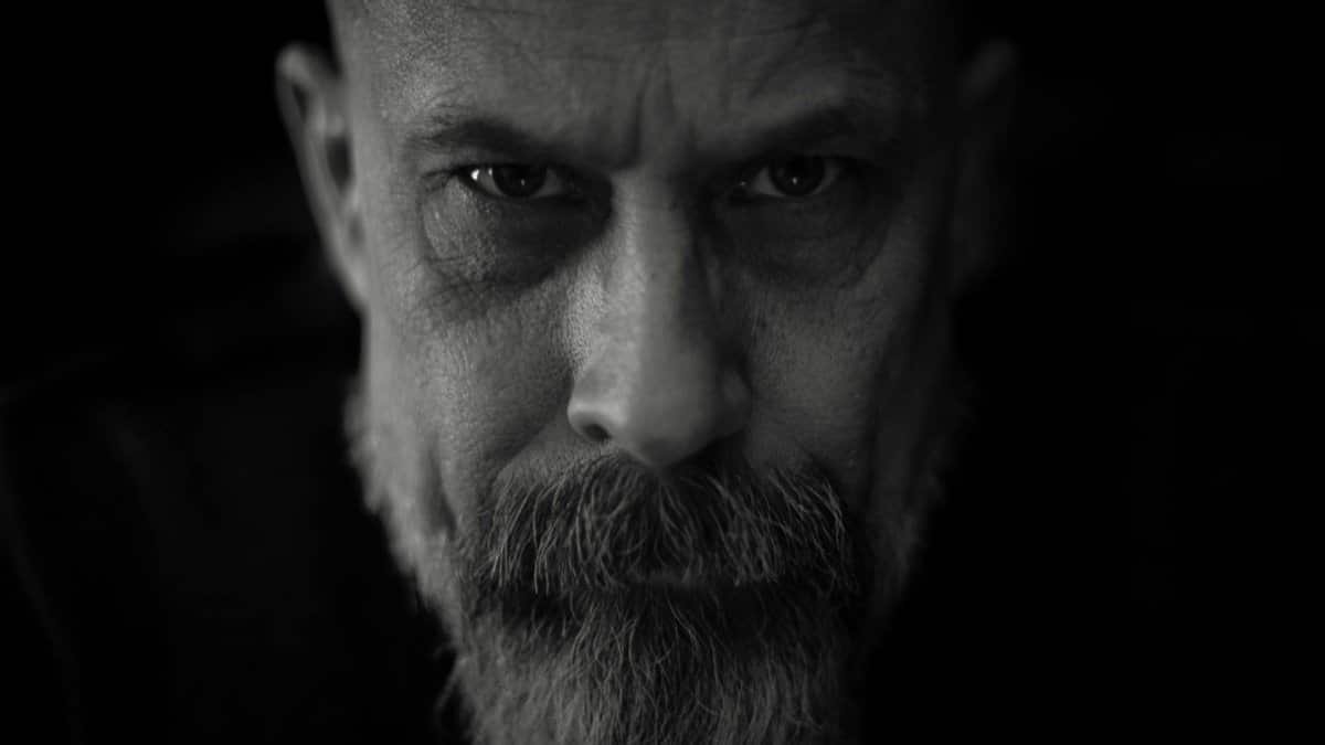 Moody black and white portrait of a bearded man with intense expression.