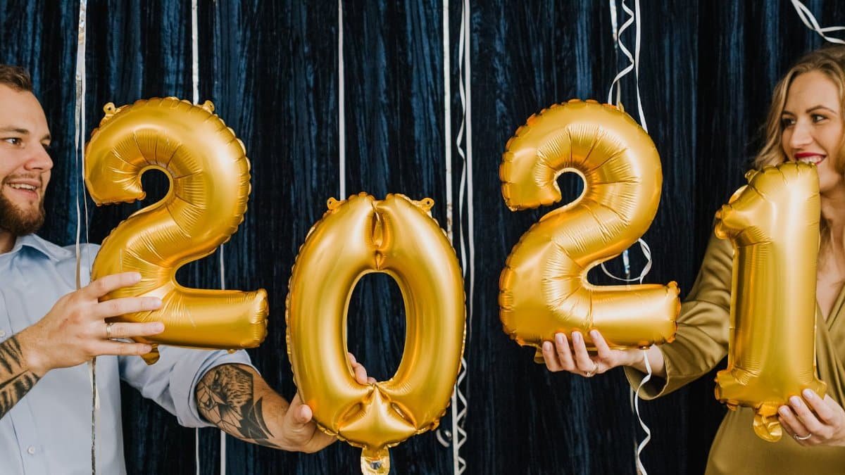 Couple holding gold balloons to celebrate New Year 2021 with smiles indoors.