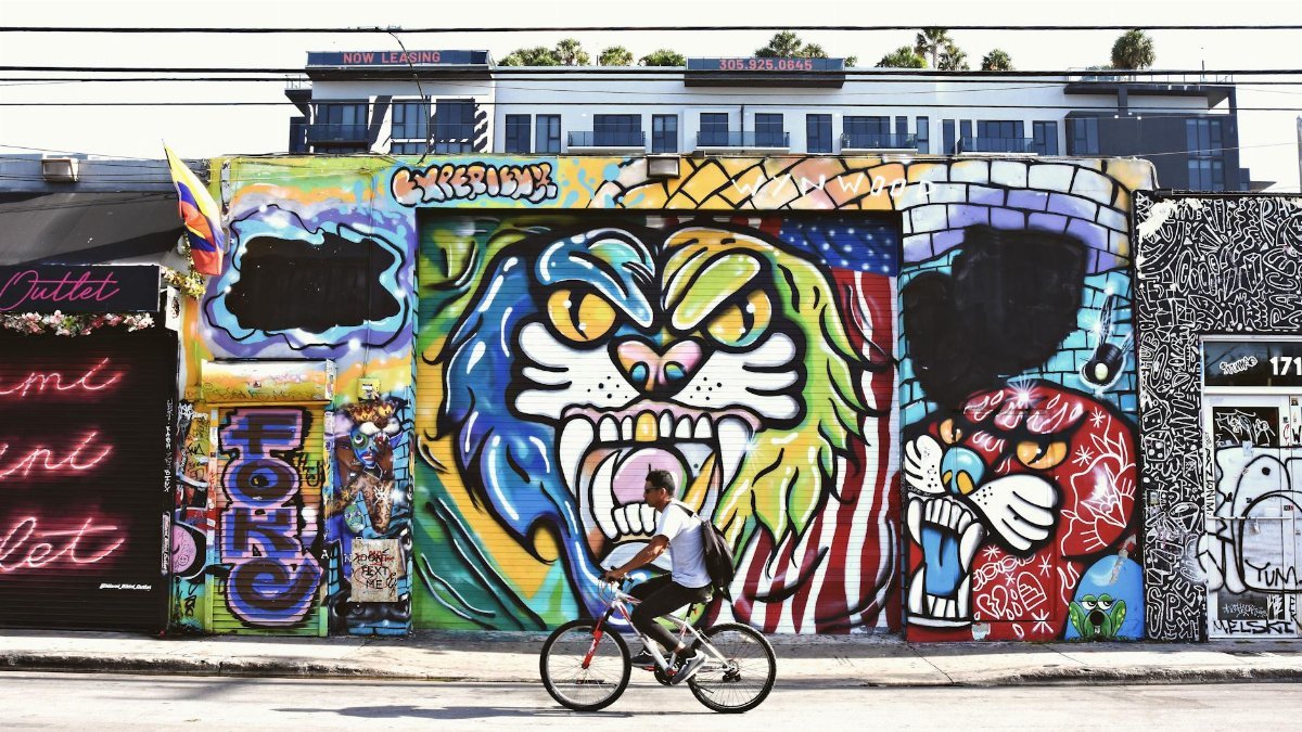 A cyclist passes vibrant graffiti on a colorful urban wall in Miami, showcasing modern street art culture.