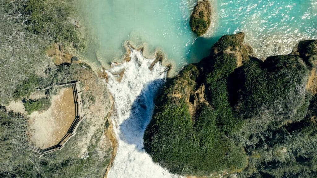 A breathtaking aerial view of a waterfall surrounded by lush greenery and turquoise water.