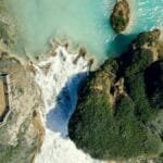 A breathtaking aerial view of a waterfall surrounded by lush greenery and turquoise water.