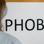 A close-up of a person holding a sign with the word 'Phobia,' illustrating mental health themes.