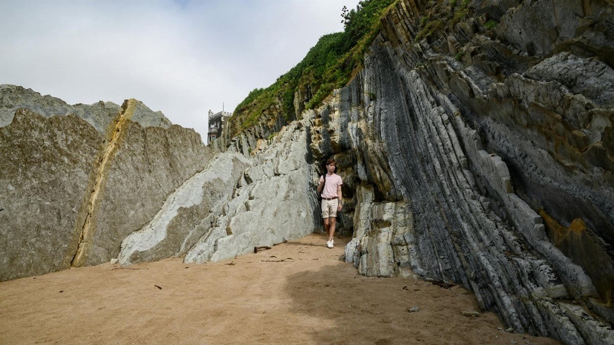 A person walks along striking cliffs in País Vasco, Spain, showcasing unique rock formations.