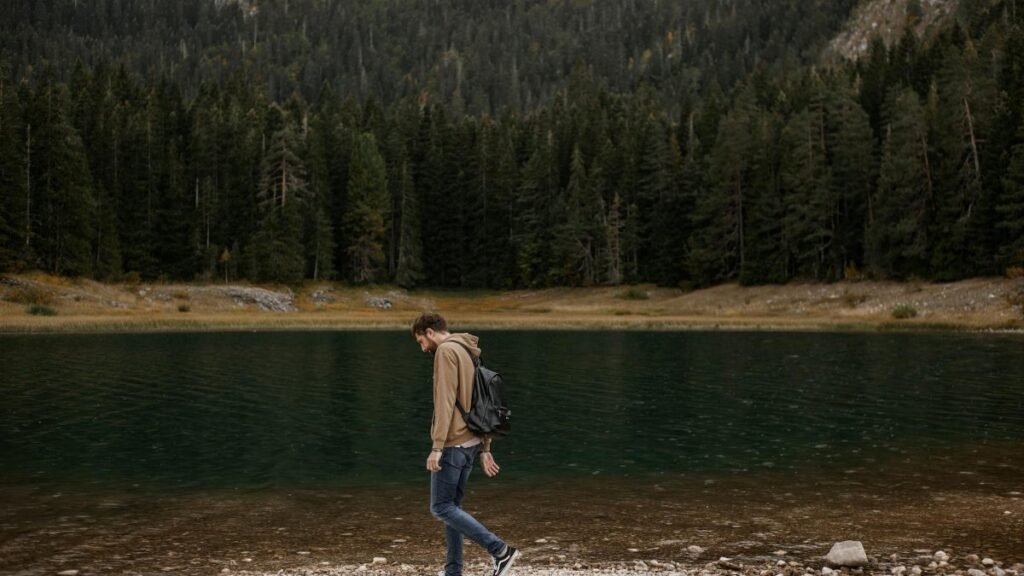 A lone man enjoys a walk by a tranquil mountain lake, surrounded by lush forest scenery.