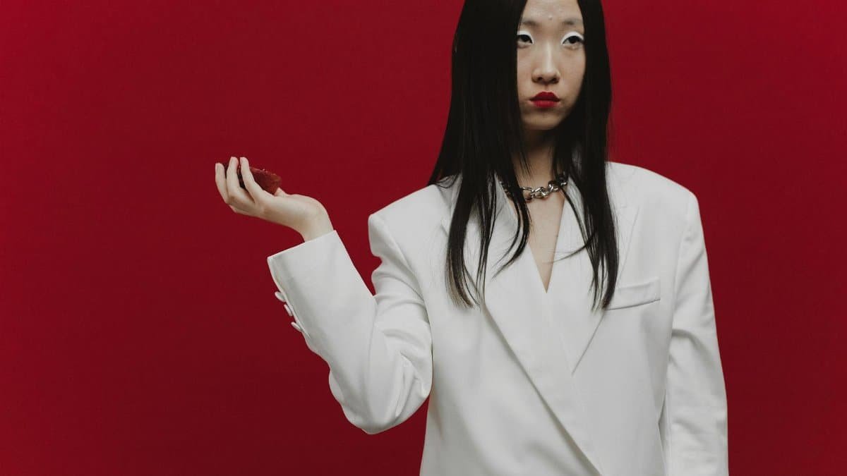 Stylish portrait of a fashionable woman in a white blazer against a red background, exuding confidence.