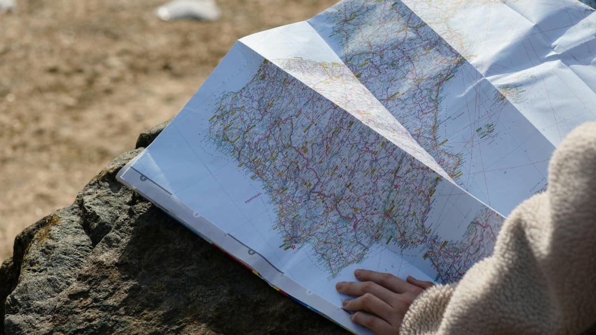 A person studies a roadmap placed on a rock, embraced by natural sunlight outdoors.