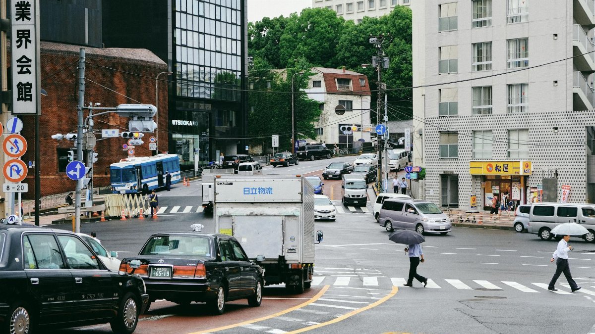 City street scene with various vehicles and pedestrians at a busy intersection.