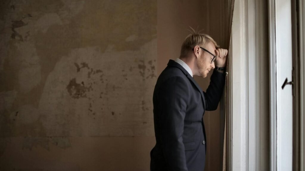 A worried businessman in a suit leaning against a window, expressing stress and concern.