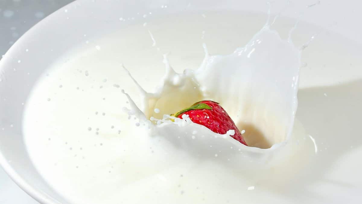 Detailed image of a strawberry splashing into fresh milk, creating a high-impact splash effect.