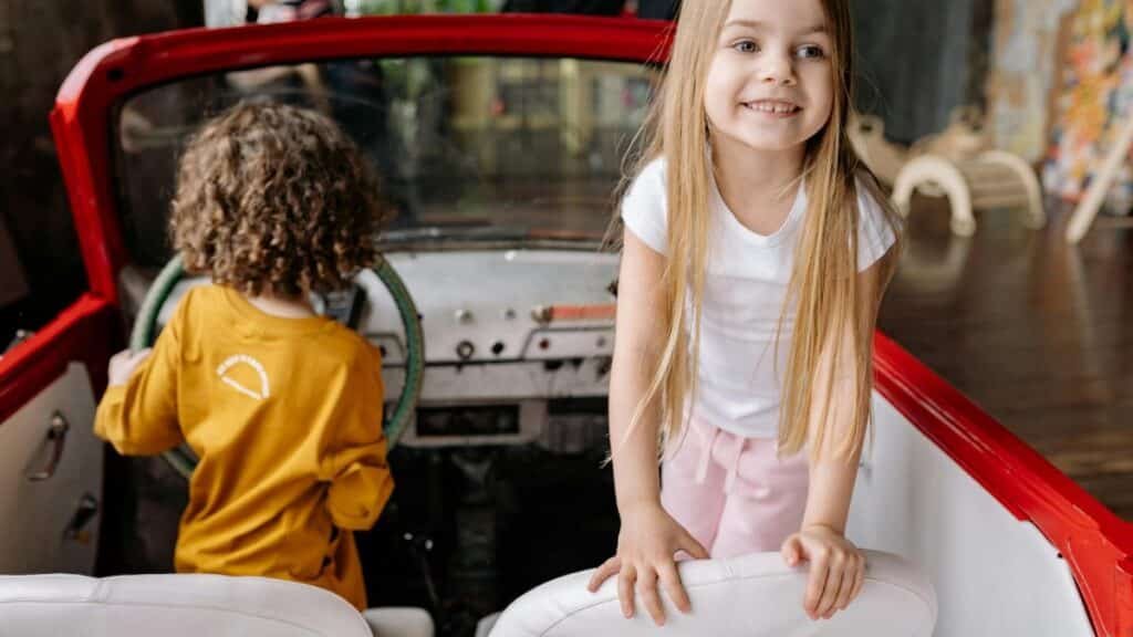 Happy children enjoying a playful moment in a classic red convertible car indoors.