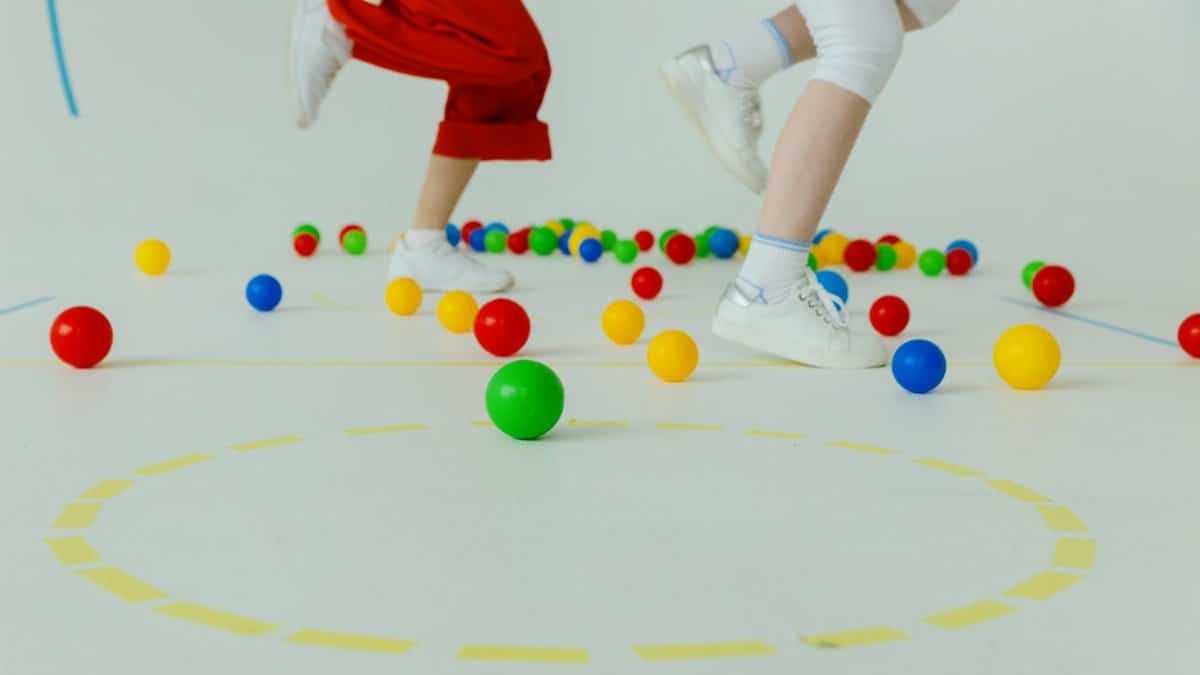 Children playing with colorful balls indoors, emphasizing movement and joy.