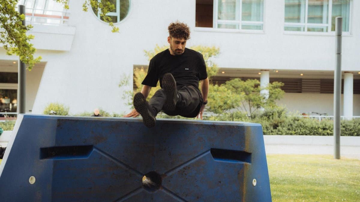 A young man skillfully maneuvers over an obstacle outdoors, showcasing dynamic parkour skills.