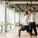 Instructor guides student in yoga pose in bright, modern studio.