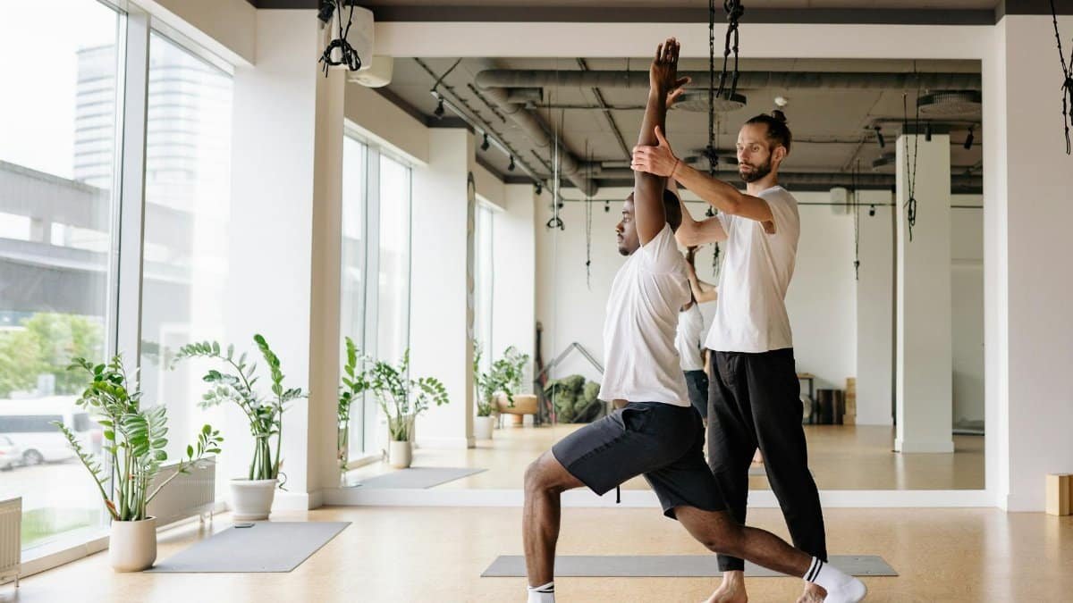 Instructor guides student in yoga pose in bright, modern studio.
