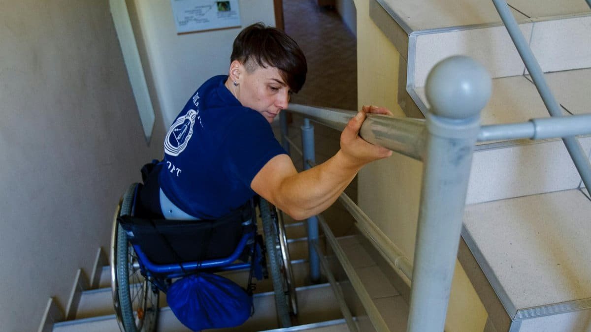 A determined individual in a wheelchair on stairs, using a handrail for support.