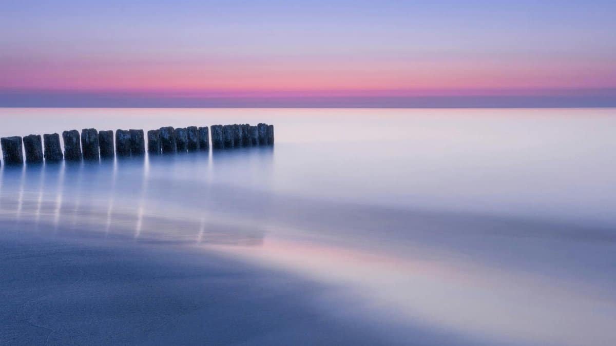 A tranquil ocean scene at twilight with soft pastels and wooden barriers stretching into the water.