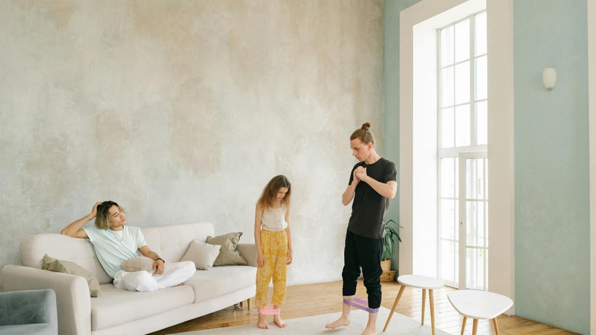 A family exercises indoors using resistance bands in a bright living room.