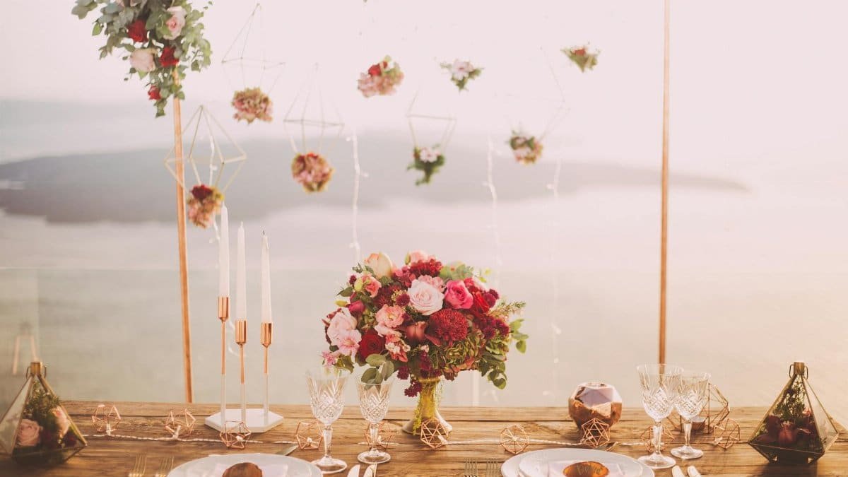 Romantic dining setup with flowers and candles overlooking Santorini waterscape at sunset.