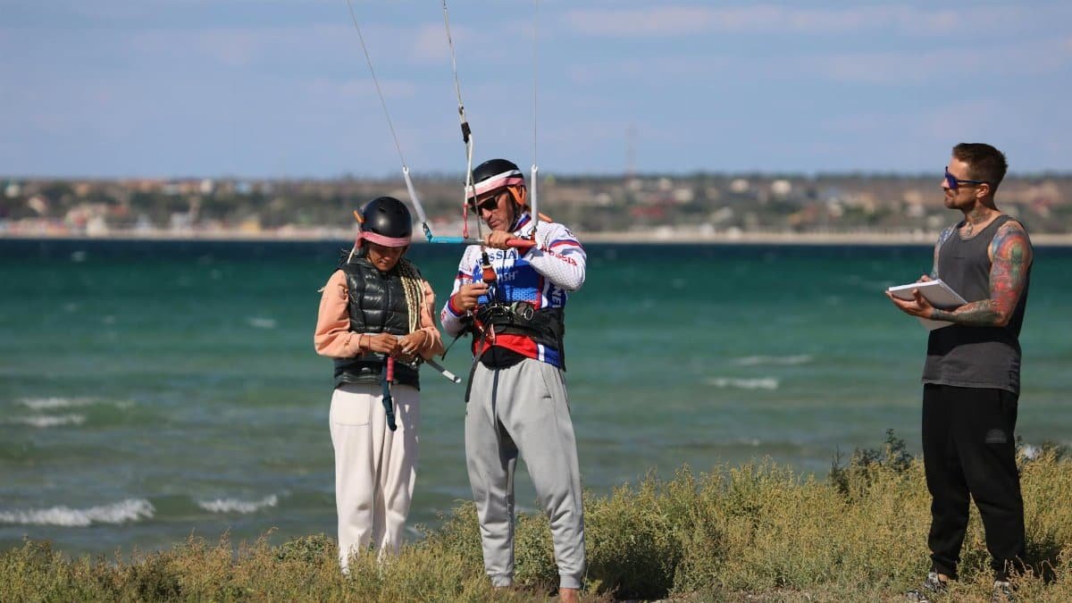 Instructors and participant preparing for paragliding on a sunny beach day.