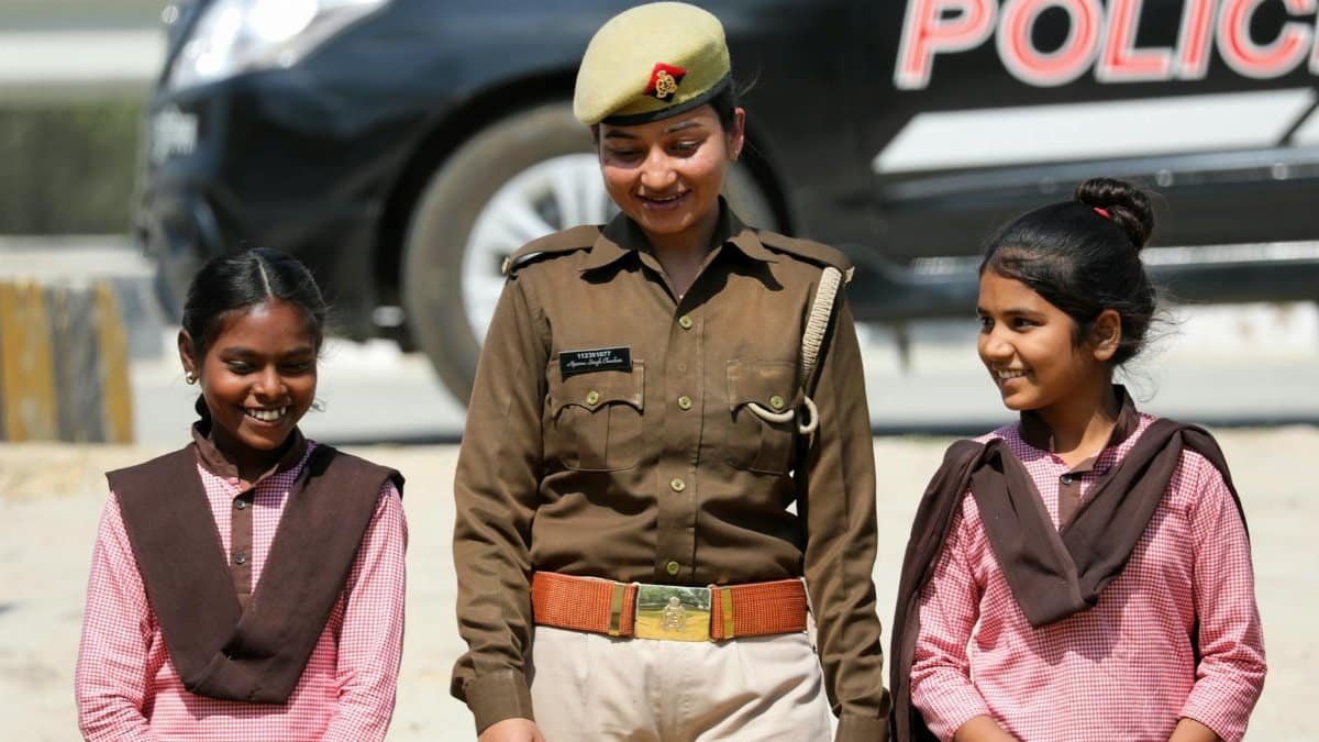 A police officer smiles while talking to two school girls outdoors.