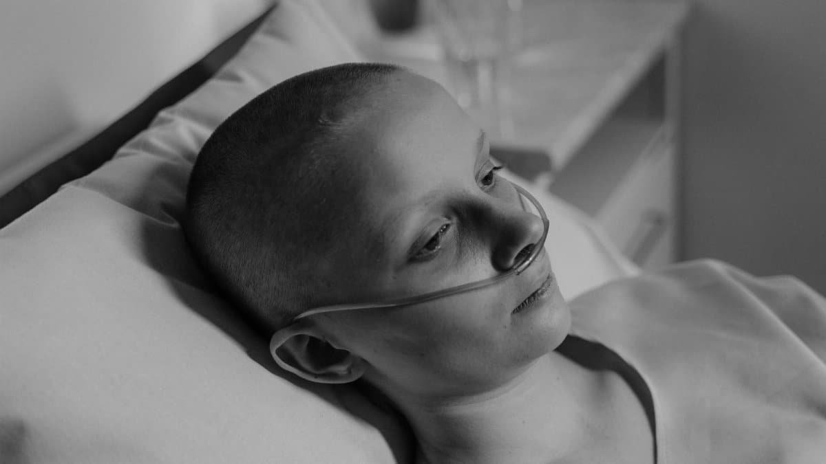 Black and white image of a woman patient in a hospital bed with a nasal cannula.