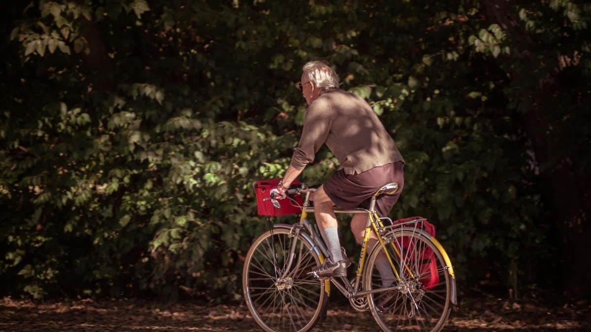 A senior man rides a bicycle on a leafy path in an autumn park.