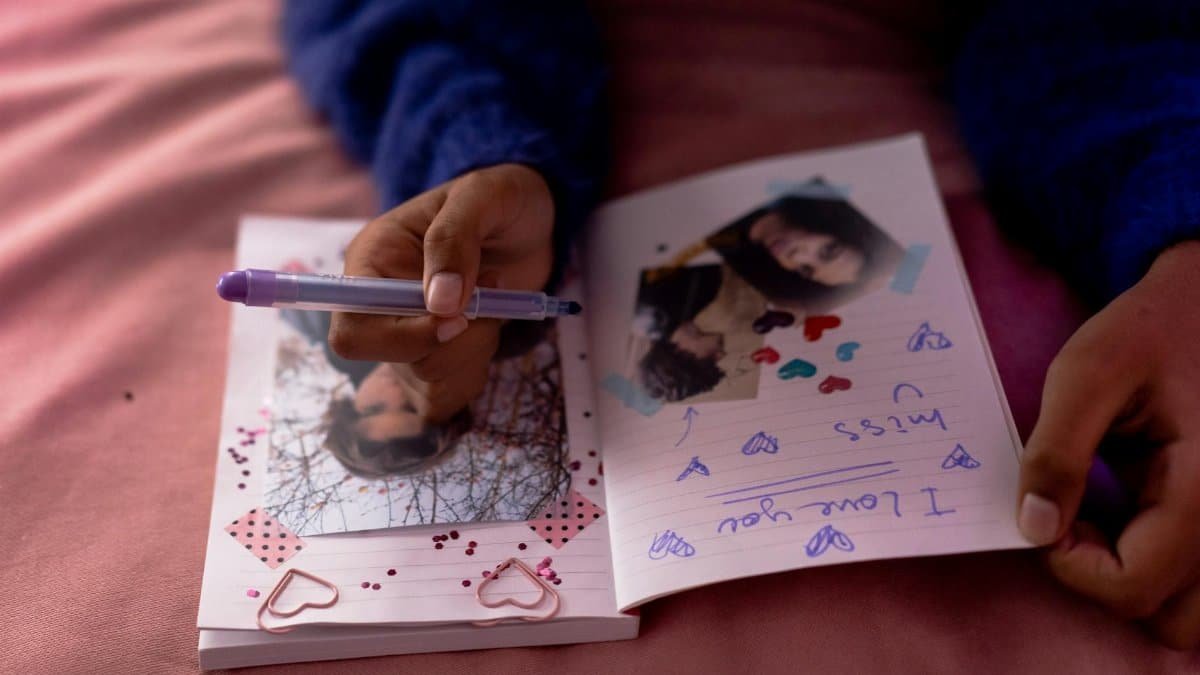 Close-up of a person writing in a personal diary with photographs and decorative elements indoors.