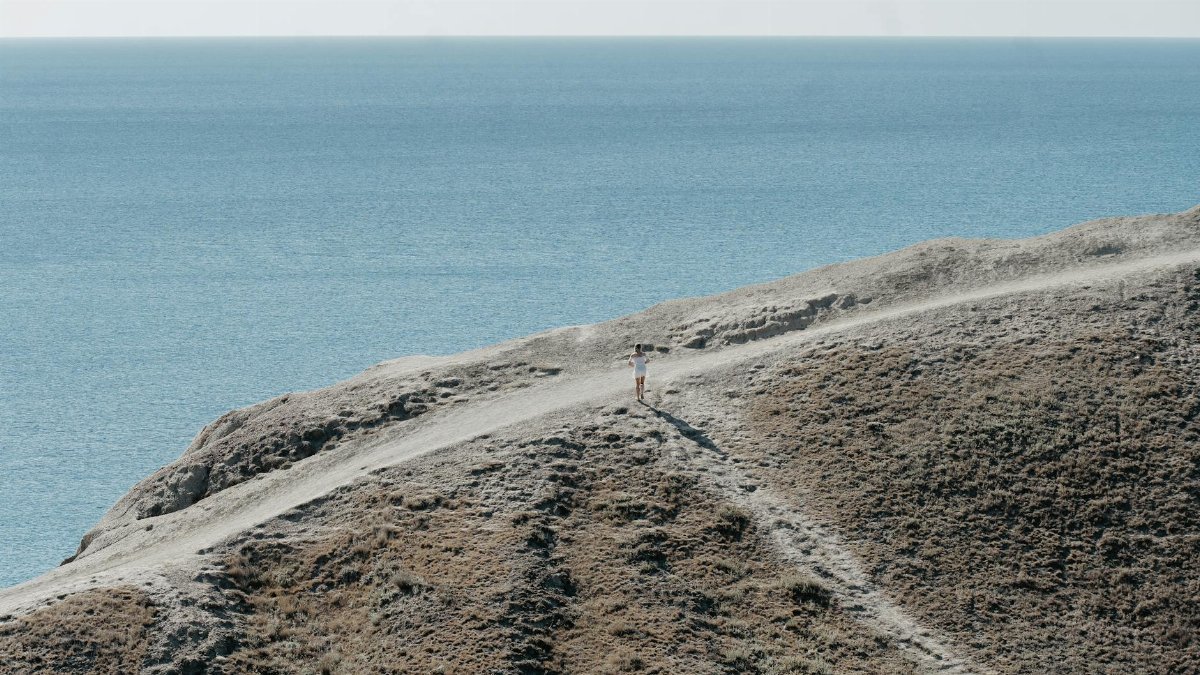 A person walking on a scenic coastal cliff path overlooking the calm sea.