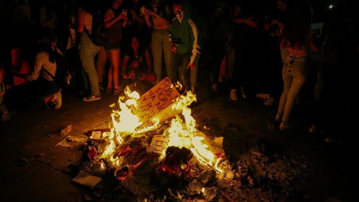A dramatic nighttime protest scene in Mexico City with a group of people around a burning fire.
