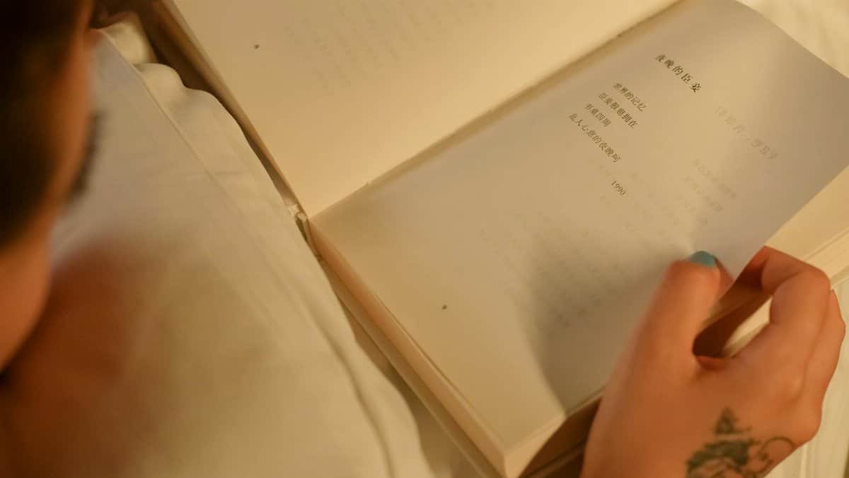 Close-up of a person reading a book indoors, showcasing a tattooed hand for a cozy and personal touch.