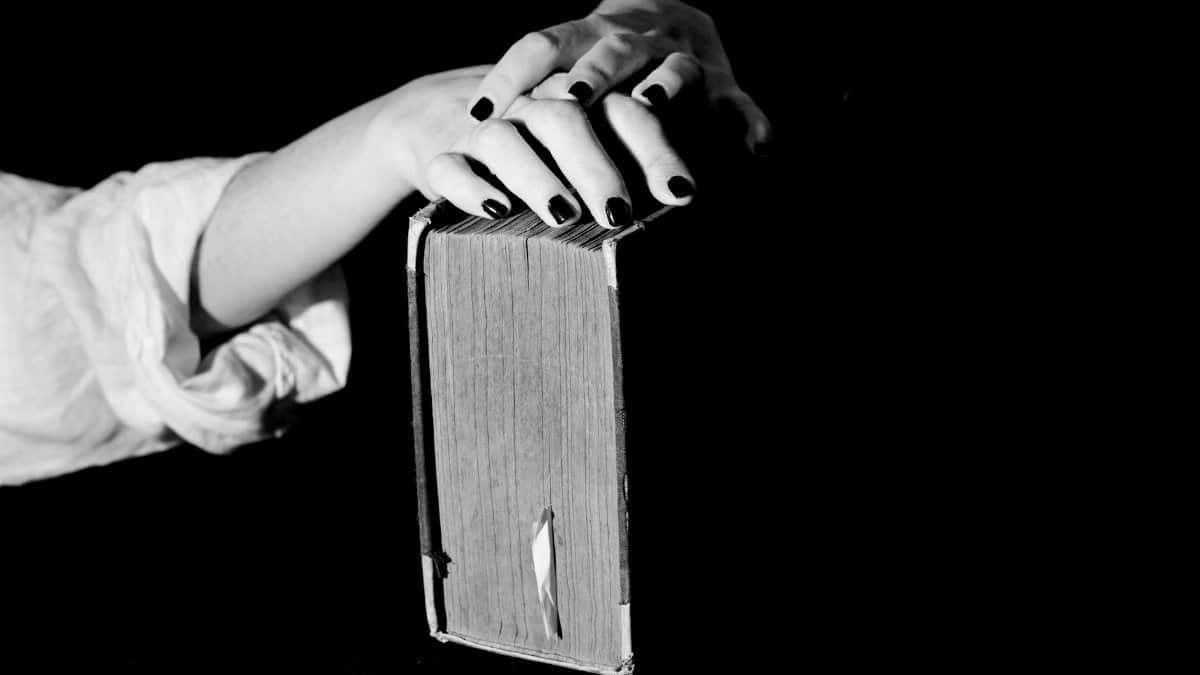 Artistic black and white photo of hands with manicured nails resting on a book.