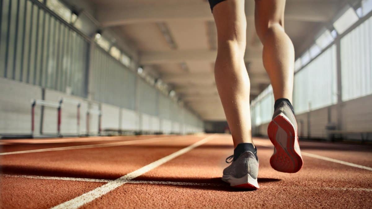 From below back view of crop strong runner walking along running track in athletics arena while doing warm up exercises during workout