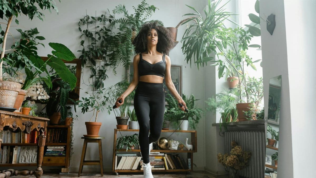 African American woman jumping rope in a plant-filled room, promoting a healthy lifestyle.