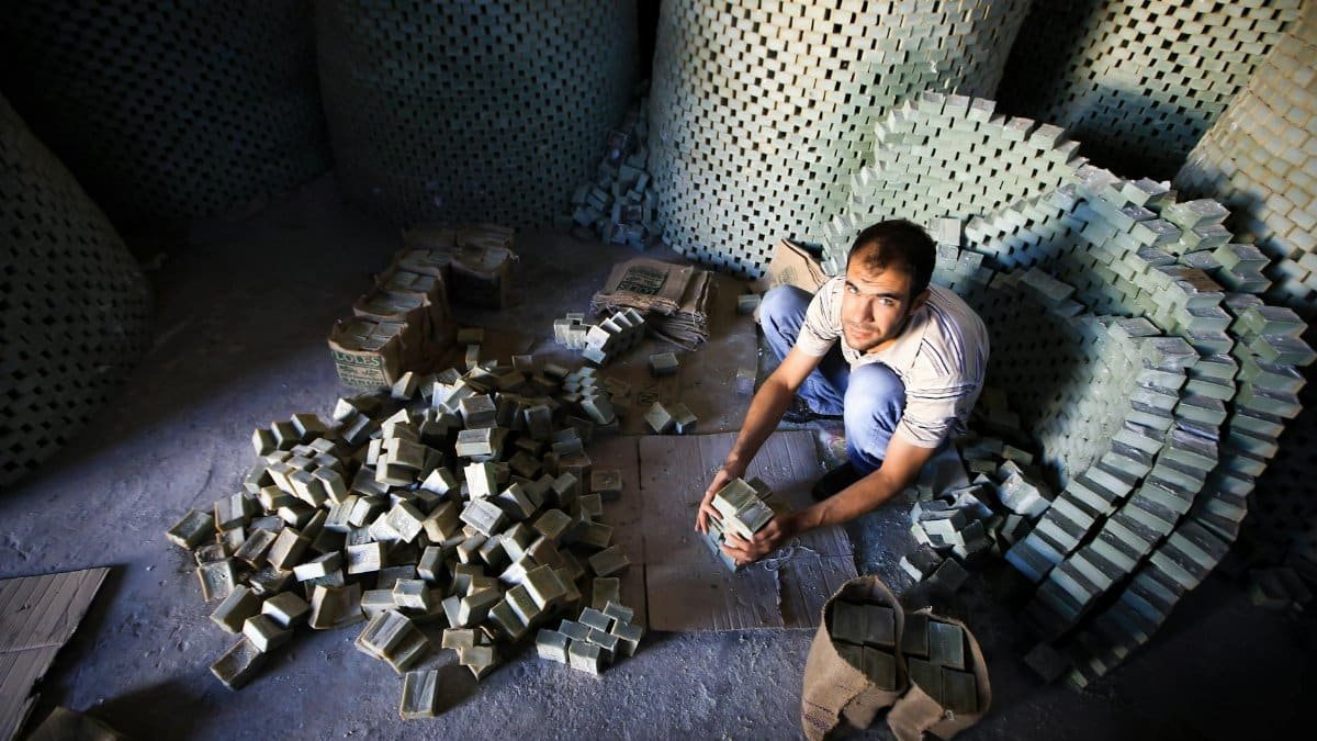 Man arranging handmade soap bricks in an industrial setting, showcasing manual labor and craftsmanship.