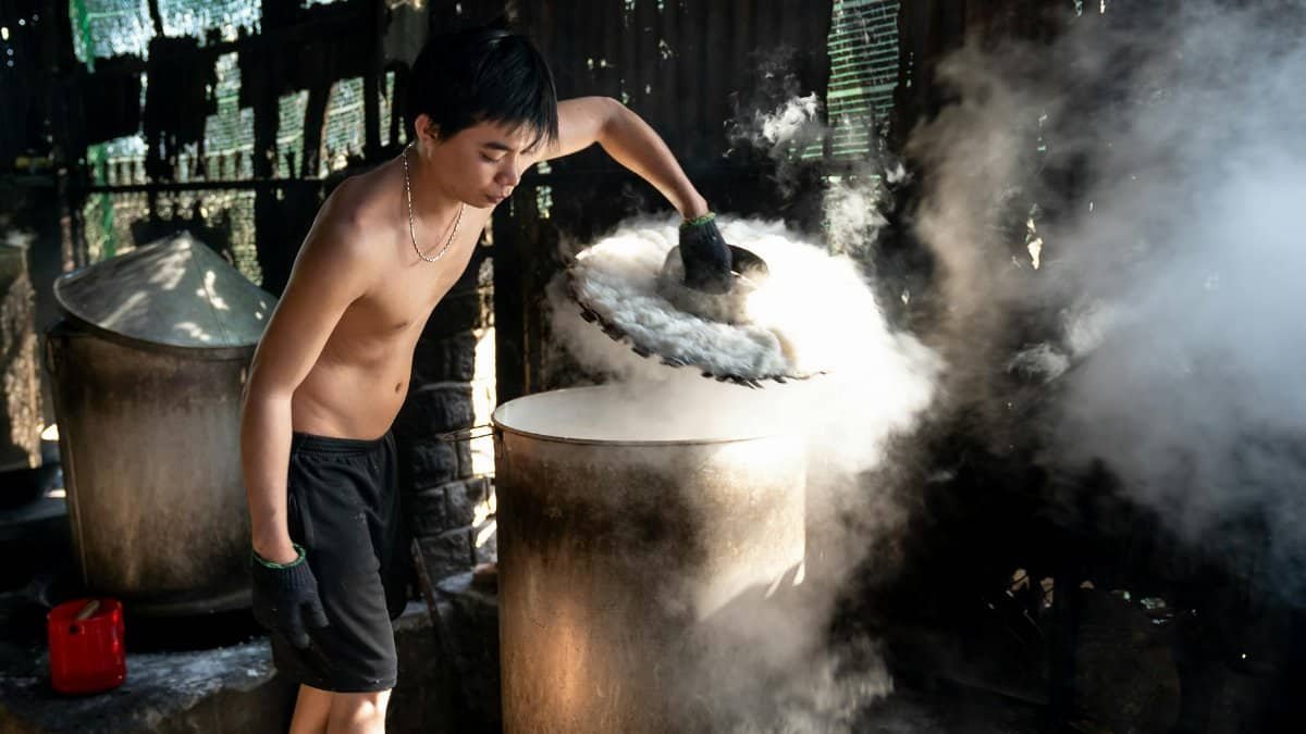 A man handling steaming containers in an industrial setting, showcasing traditional processes.